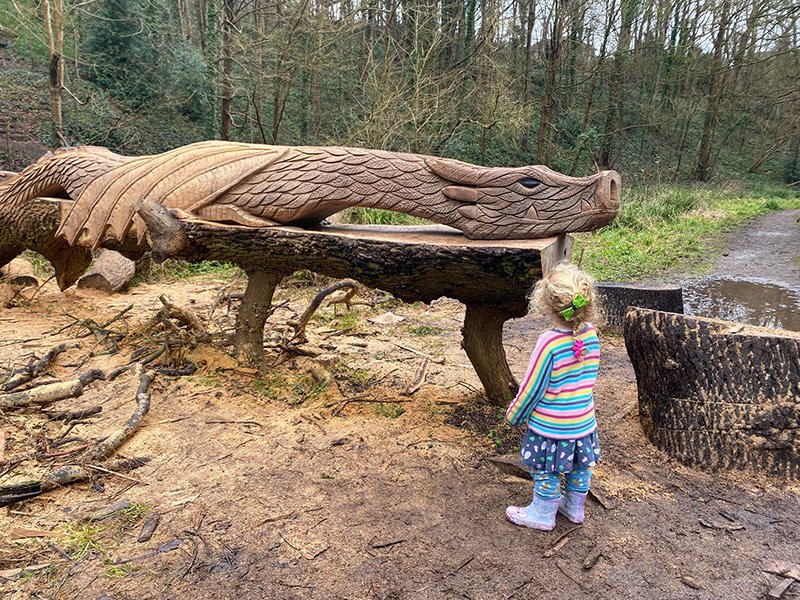 A blonde-haired child looking up at a wooden dragon sculpture